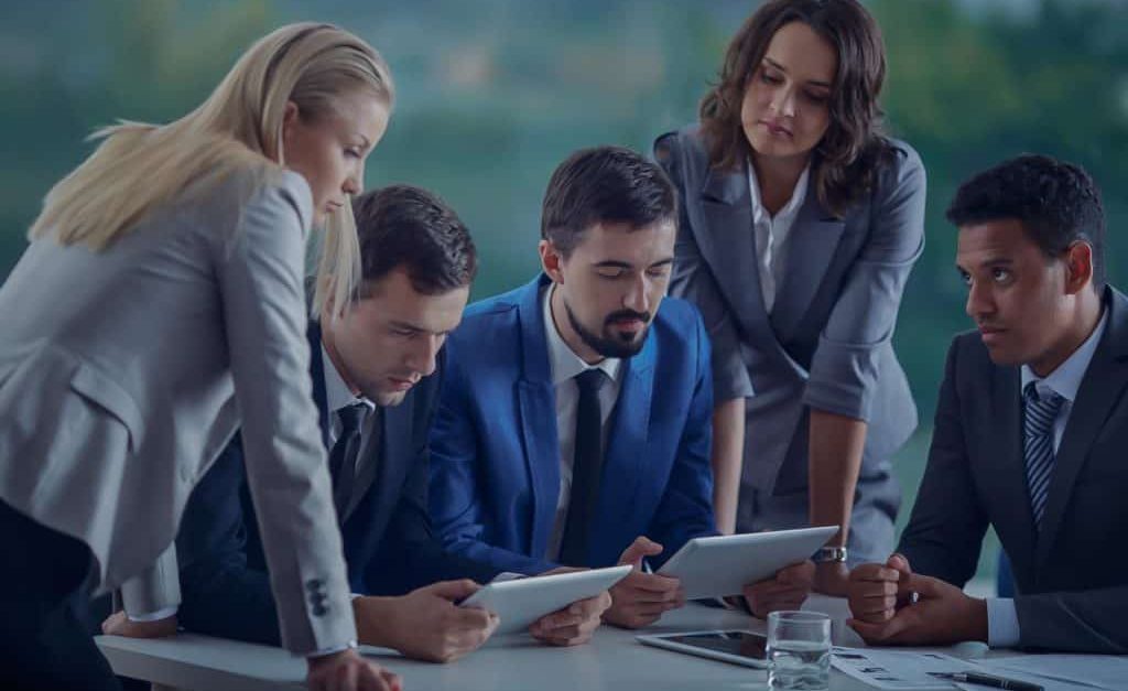 group of 5 people dressed in suits all looking at a tablet