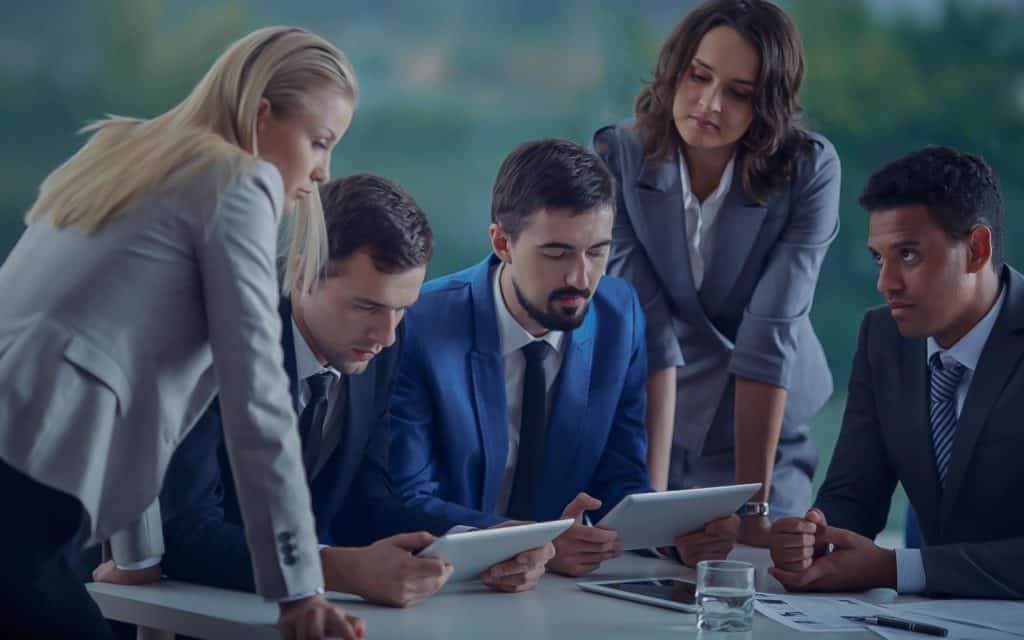 group of 5 people dressed in suits all looking at a tablet