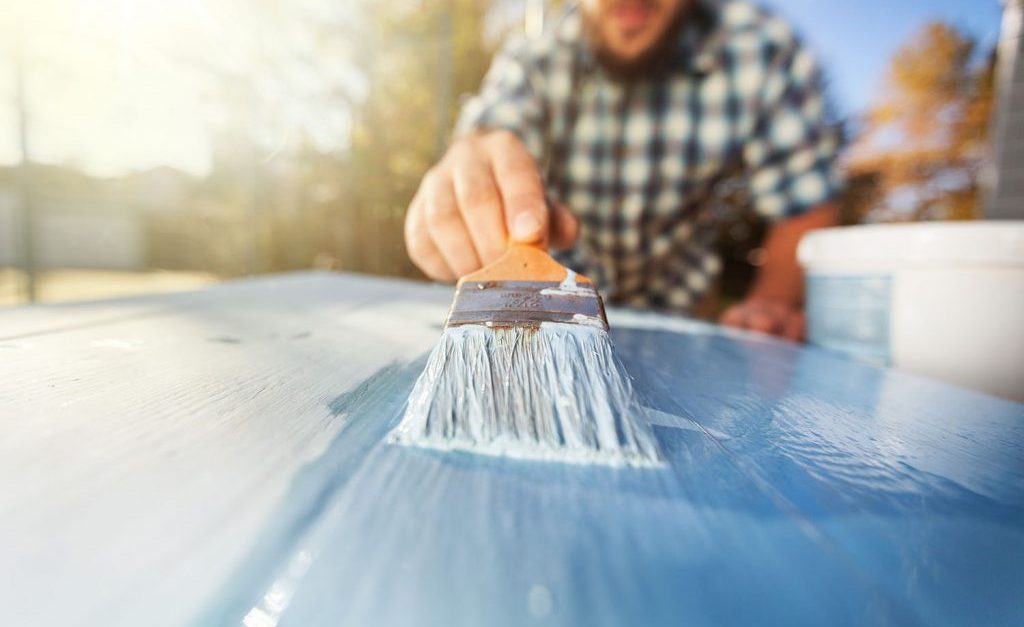 man painting a piece of wood with blue paint