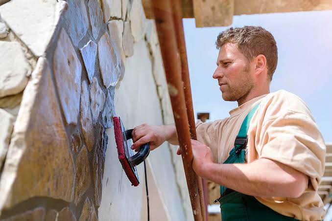 man laying bricks on the side of a house while standing on a latter